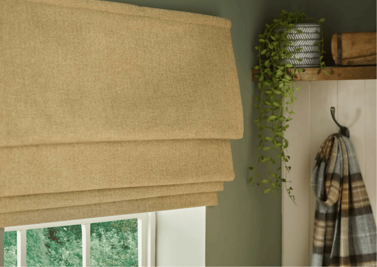 Brown roman blind on a window with a plant and plaid fabric in the background.